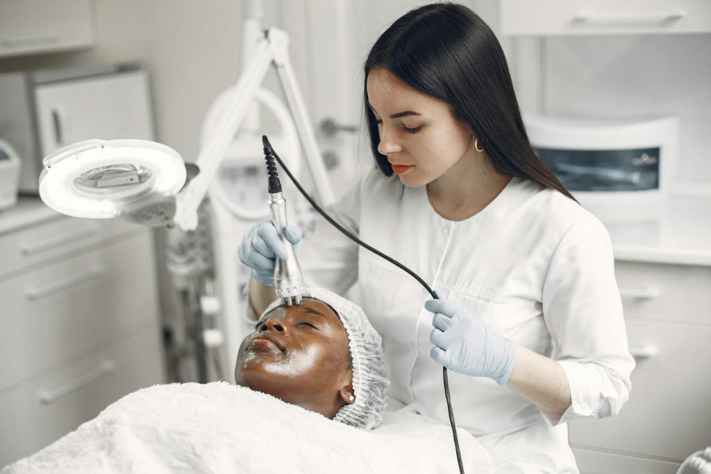 Dermatologist examining patient skin condition with magnifying lamp at Elect Dermatology clinic in New Braunfels TX